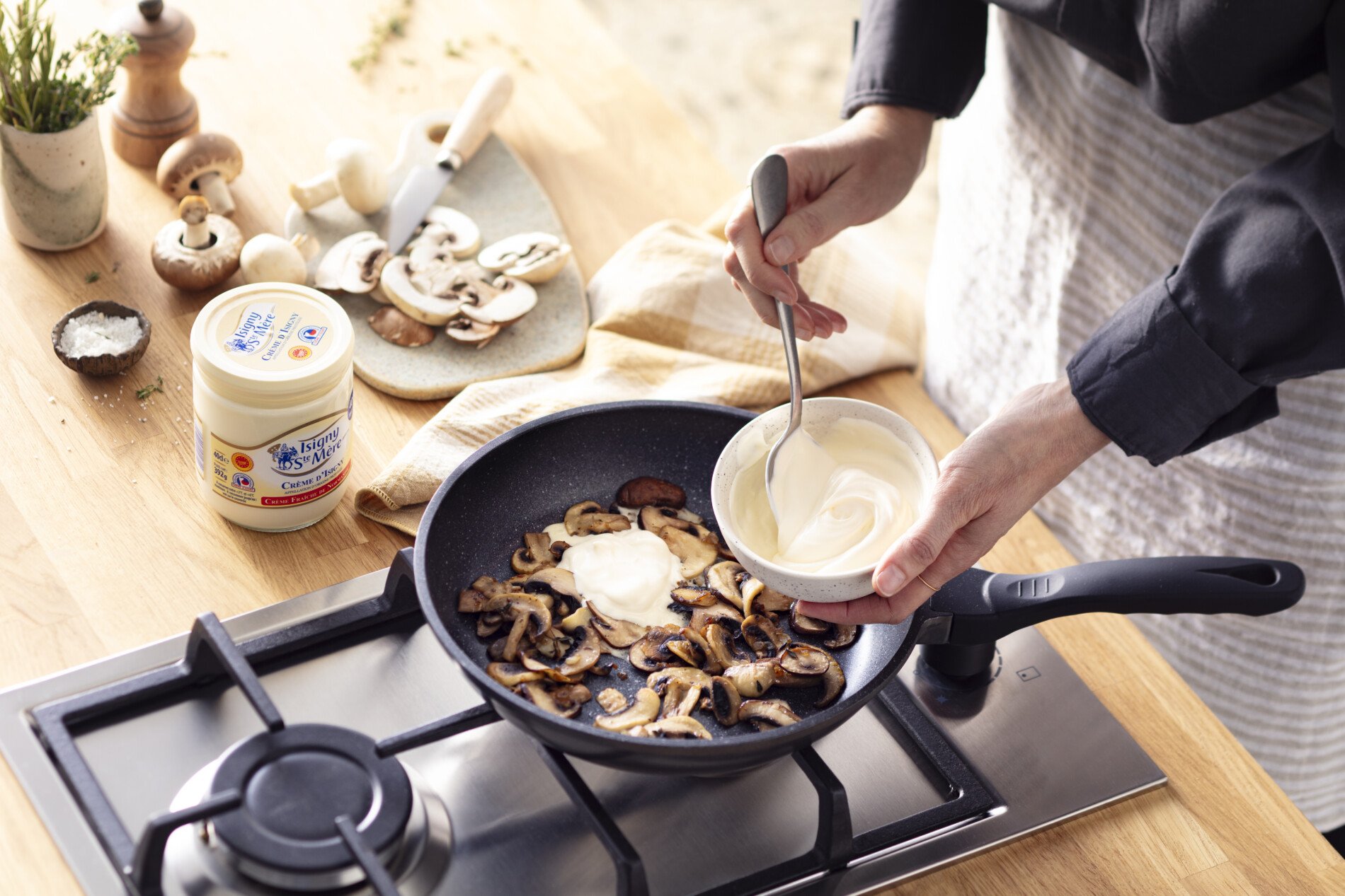 Personne en train de cuisiner des champignons avec de la Crème Isigny Sainte-Mère dans une poêlé 